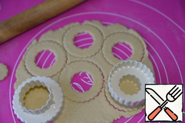 Take out the dough from the refrigerator, for convenience, divide in half, the second part again put in the refrigerator. Roll out with a rolling pin in a layer 5 mm thick. with the help of cuttings, we make round cookie blanks. Make a hole in the middle. You can use glasses, glasses.