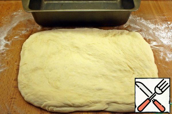 Take a form for bread, grease with oil. The dough will greatly increase in volume, so do not take a small form. I have a cake tin 23*13*7. If you have less molds, then take two. Next, we dust the work surface with flour, from the dough we form a rectangle about the length of the form.