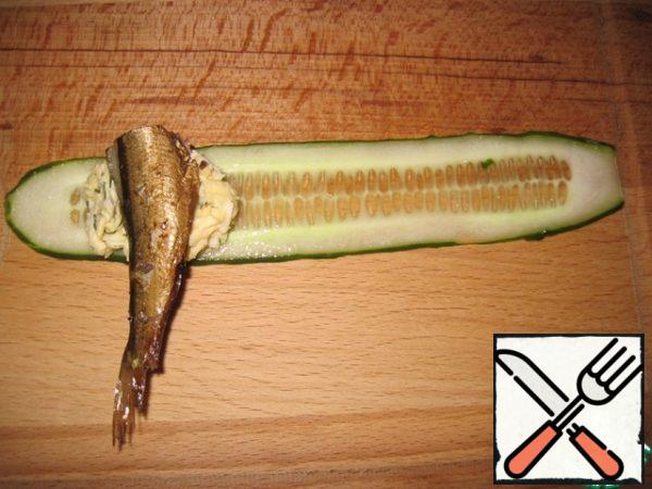 Using a peeler, cut the cucumber into thin plates. Put a teaspoon on the edge of the cucumber strips filling. Put one fish on the filling.
It is desirable that sprats were small in size. If the fish are too large, you can trim them.