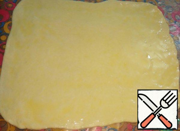 Roll out the dough into a thin rectangle, dusting with a little flour. The thinner it is, the more layered it will be.
Grease with melted, cooled butter.