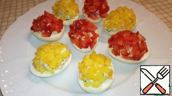 Cut the red and yellow peppers into small cubes and sprinkle them on top of the eggs, pressing them down a little.