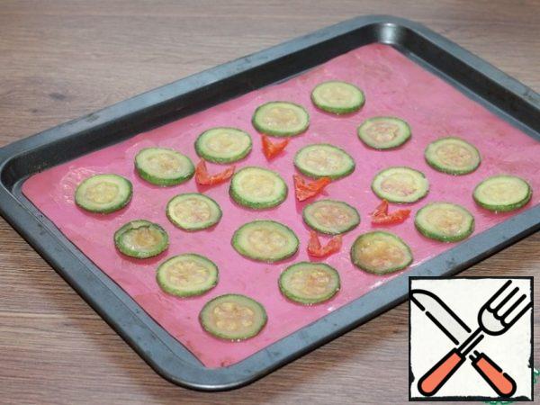 With zucchini drain the liquid and spread on a paper towel. Cover the baking sheet with a silicone baking Mat and grease it with oil. Arrange the zucchini slices and a little pepper.