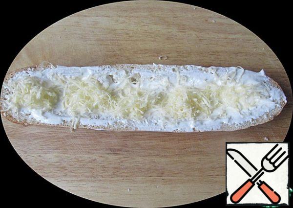 Half of the baguette smeared with mayonnaise and sour cream mixture.
One half, the bottom, sprinkle with grated cheese so that the cheese gets to the edges.