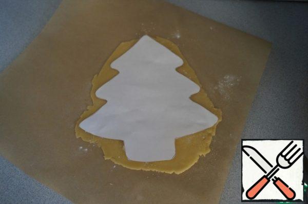 Divide the finished dough into 3 parts and roll each into a thin layer. Cut out the Christmas tree according to the template. Prick the cake with a fork so that it does not swell during baking.