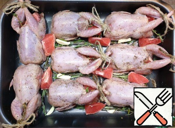 Put the quail on a baking sheet, distribute the remaining grapefruit (orange), garlic, thyme or rosemary sprigs between them.
Pour each bird with a tablespoon of vegetable oil.
Cover the baking sheet tightly with foil and put it in a preheated 180 * C oven for 35-40 minutes.