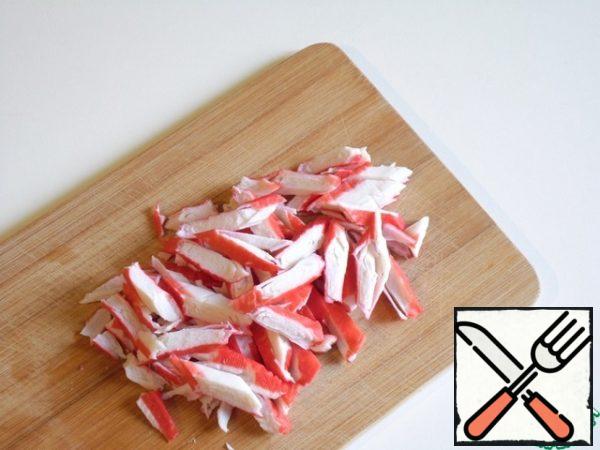 Crab sticks should be taken chilled. If you have frozen ones, let them thaw well, then blot them on paper towels as hard as possible.
(weight, which in stores in bulk in trays, just do not fit, there is only a smell of starch from the promised fish scraps!)
Chop sticks at an angle, 5-7 mm wide.