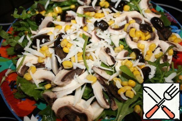 On a wide dish, spread the arugula and mushrooms.
Sprinkle with corn and olives.
RUB the cheese.
