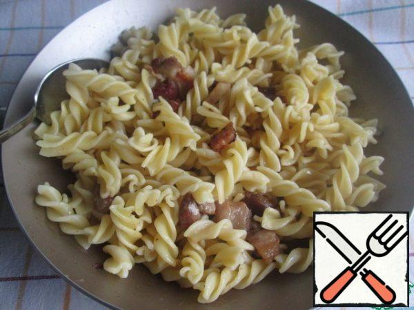 Cut the bacon into slices (if the strips of bacon are thick, then cut into cubes) and fry in a dry pan.Boil the macaroni in salted water according to the instructions on the package, then drain the water and place it in the pan with the finished bacon. Stir well.