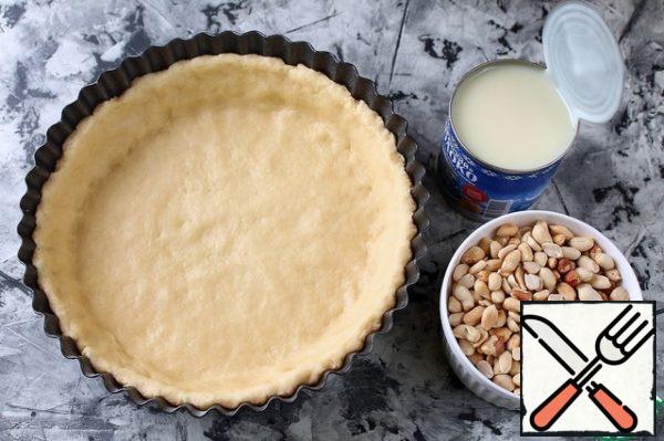 Fry the peanuts and peel them.
Put peanuts on the dough, add salt and pour condensed milk on top.