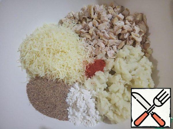 Put mashed potatoes from boiled potatoes, cheese grated on a fine grater, chopped chicken meat, 1 tablespoon of flour, 3 tablespoons of breadcrumbs, paprika, salt and ground black pepper to taste in a deep bowl - and mix well.
