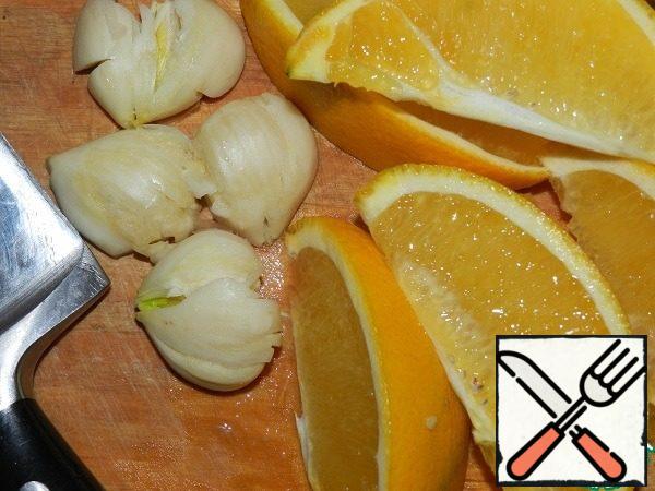 Wash the orange. Cut into slices. Crush the garlic cloves with the flat part of a knife.