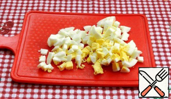 Boil the eggs, cool them, peel them, and cut them into cubes.