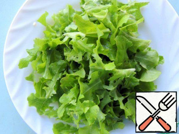 Lettuce leaves are torn by hand into small pieces and placed on a plate.