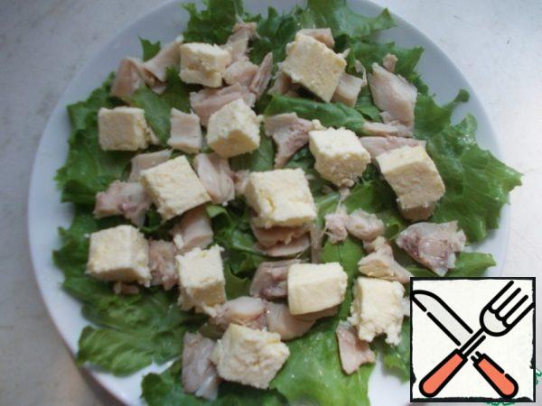 Clean lettuce leaves are torn with your hands and put on plates, on top of pieces of chicken and cheese cubes.
