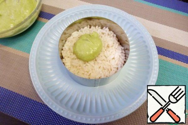 The salad is collected in layers. The first layer is cooked rice. Grease this layer with the prepared avocado dressing with garlic.