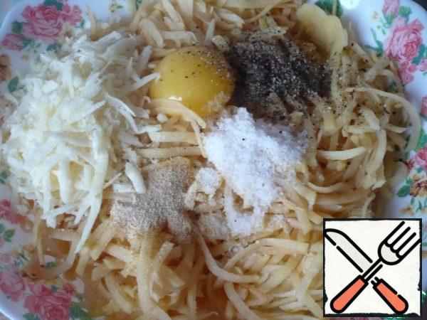 Transfer the chopped potatoes to a kitchen towel to squeeze out the juice. Then put the pressed potatoes in a large bowl, add the egg, salt and ground black pepper to taste, onion powder, garlic powder and crushed Parmesan cheese 50 grams.