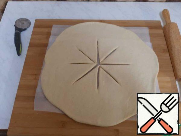 Roll out the dough on parchment into a circle with a thickness of 5-7 mm. In the middle make cuts.