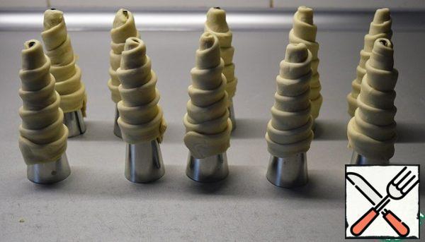 Grease the aluminum molds with oil. Fold the dough strips in half lengthwise and screw them onto the prepared cones.