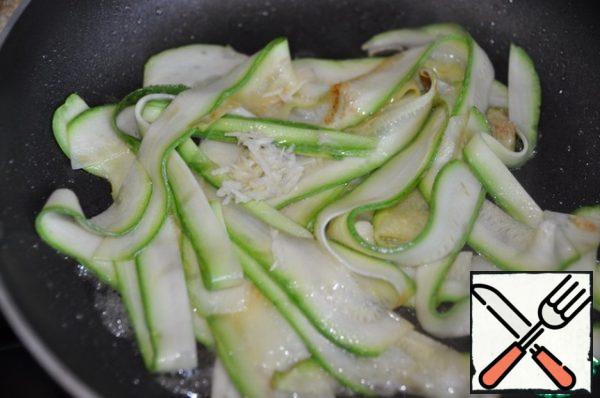 Pour vegetable and sesame oil into a hot frying pan and put the zucchini noodles. Fry for 5 minutes on high heat until transparent, stirring constantly. Add the chopped garlic.