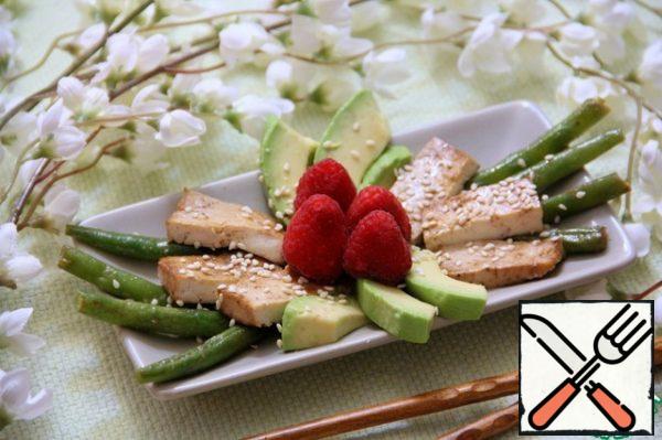 Cut the finished tofu into portions. Place the avocado on a plate in the center, followed by the tofu and the bean pods around the edges. When serving, sprinkle with sesame seeds and decorate with raspberries.