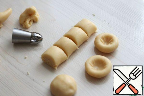 From the second part of the dough, form balls in which, with the help of a pastry cream nozzle, make depressions.
