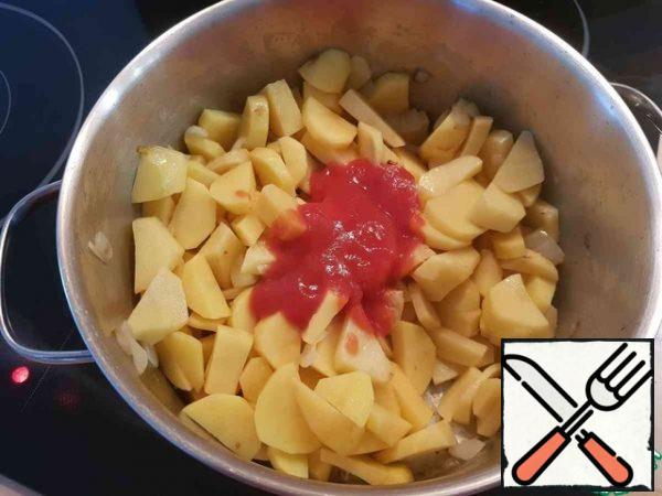 Add the potatoes to the onion, pour out the tomato paste, add the sweet paprika, mix everything well, leave on a low heat and put out for a couple of minutes.