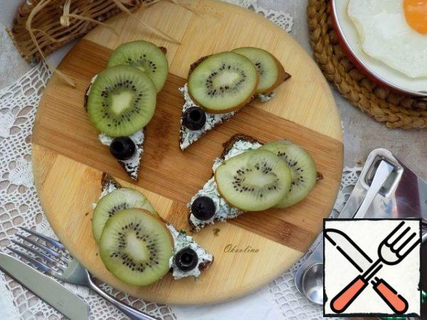 Generously spread the bread with cheese and herbs, lay out slices of kiwi and, if desired, add olives. The toast is ready!