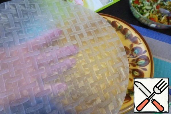 Dip a sheet of rice paper in water poured into a wide plate for 10 -15 seconds, it should remain slightly firm. Place it on a wooden board moistened with water. On the board, the sheet will finally soften, and it can be rolled into a roll.