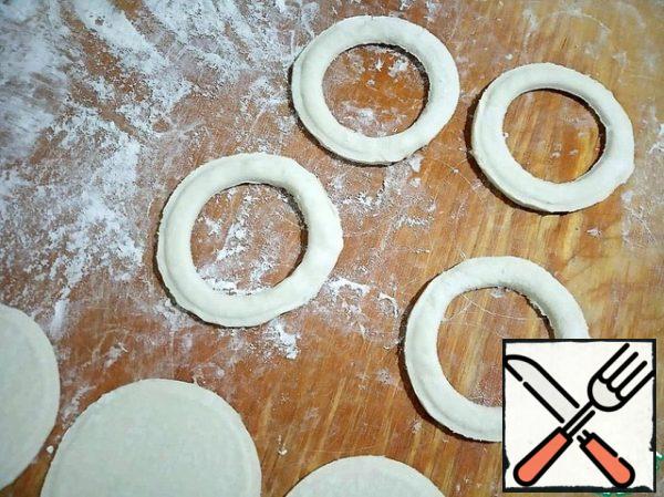 Now use the remaining pieces of unrolled dough. We squeeze out of them the same number of circles as the first time. Then squeeze out the middle and remove. And we get these kind of rings. (I used glasses of different diameters).