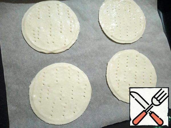 Spread the circles of dough on a baking sheet covered with parchment paper. Often prick with a fork (so that the dough does not rise very much when baking) and grease with protein to fasten the lower and upper layers of the dough.