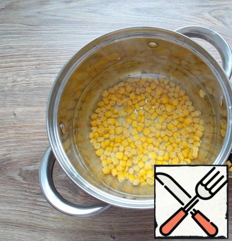 Pour water into a pot and put it on the fire, bring to a boil. Drain the liquid from the corn and add it to the pan with water.