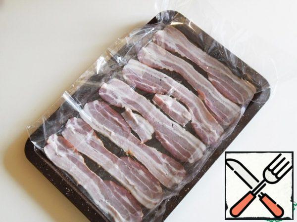 I took the sliced bacon. Cut the baking bag on the sides and put one half on the bottom of the baking tray, spread out the bacon slices and cover the other half of the bag.