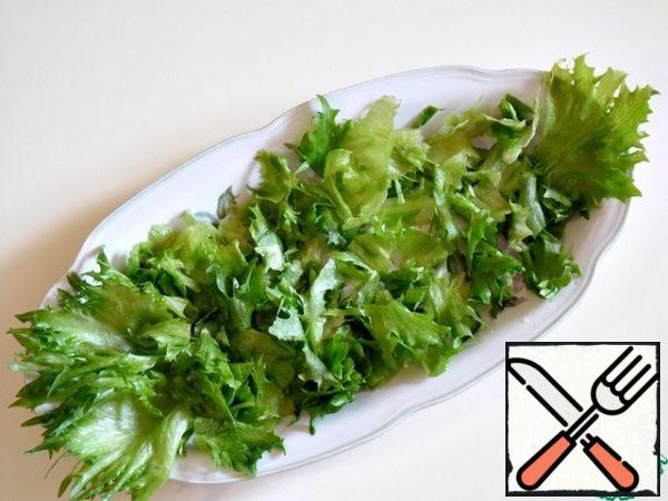 Leaf lettuce is randomly picked into pieces, put on the bottom of a salad bowl or dish for serving.