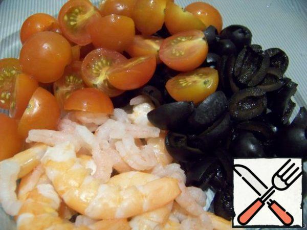 Pour boiling water over the prawns, drain the water in about five minutes. I have them of various sizes, there were a few small ones that were cleaned, and I added large ones, Royal ones. Cut the olives in halves. Cherry tomatoes are also cut in half.