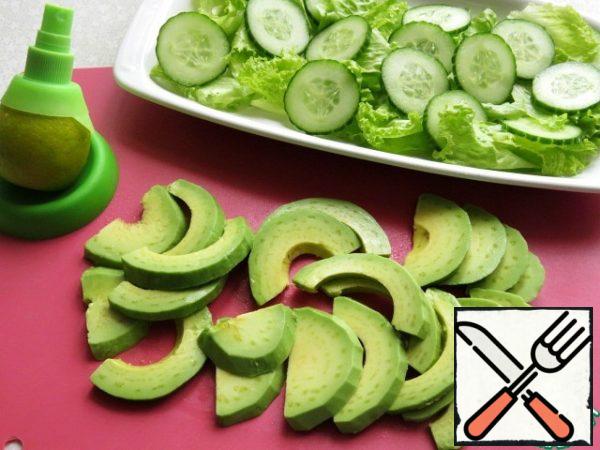 Clean the avocado, remove the stone, cut into slices and sprinkle with lemon juice, so that the avocado does not darken. Spread it on top of lettuce and cucumber leaves.
