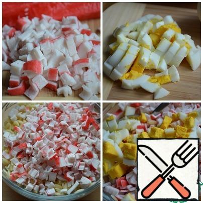 Boil the egg, peel it, and cut it into small cubes. Cut the crab sticks into small cubes. Add the egg and crab sticks to the pasta.