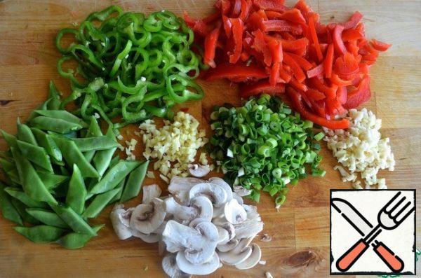 Wipe the mushrooms clean with a napkin and cut them into medium-thick plates. Red and green pepper thinly cut. Cut the green onions into thin rings. Finely chop the garlic and ginger. Remove the leg from the bean and cut it into 3-4 parts, depending on the length.
