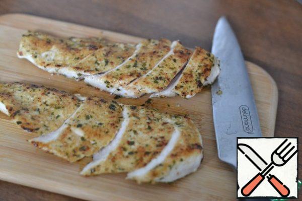 The finished tender chicken breast fillet is laid out on a board and cut into strips.