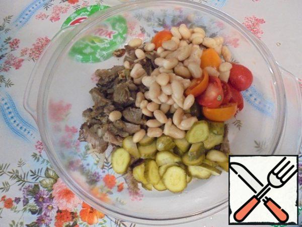 Put the salad ingredients in a bowl:
pickled cucumbers, fried onions with lamb, canned beans, cherry tomatoes.
Stir.