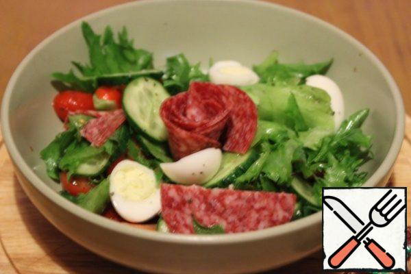 Add sliced cucumber, tomatoes, cherry, quail eggs and sausage slices cut in half to the lettuce leaves. Season with salt and pepper and olive oil.
