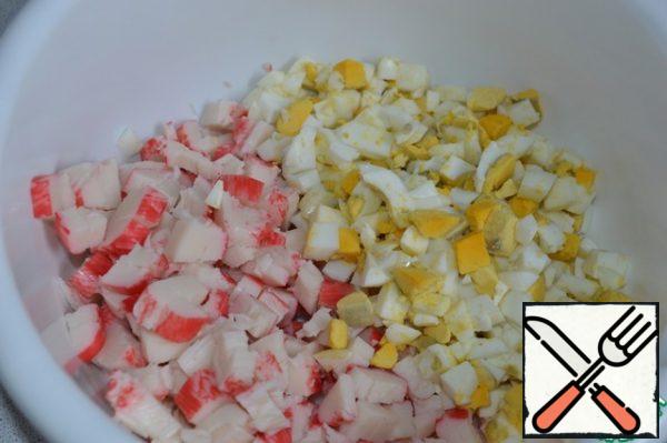 Cut the crab sticks and boiled eggs into cubes and put them in a salad bowl.