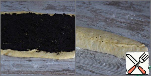 Put the dough on the work surface, lightly sprinkled with flour, knead, roll out in a rectangle measuring 25 by 40 cm.
Evenly spread the poppy mass on the dough, stepping back a little from the edges. Roll the dough layer with poppy seeds into a roll. Pinch the seam.