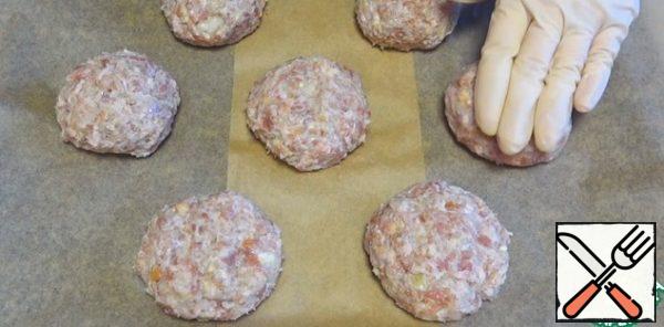 I form round cutlets from minced meat. I put them on a baking sheet covered with parchment. Slightly press down.
