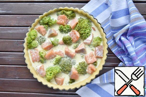 Take the cooled dough out of the refrigerator and roll it out according to the diameter of the mold. Use a rolling pin to transfer the dough and distribute it on the bottom and sides of the mold. Cut off excess dough. Spread out the pieces of salmon alternating with broccoli inflorescences, pour the prepared filling.
