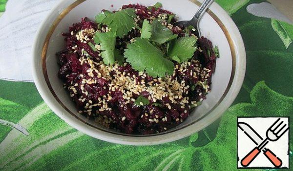 Spread the beet salad in a salad bowl, sprinkle with sesame seeds, and decorate with a sprig of coriander.