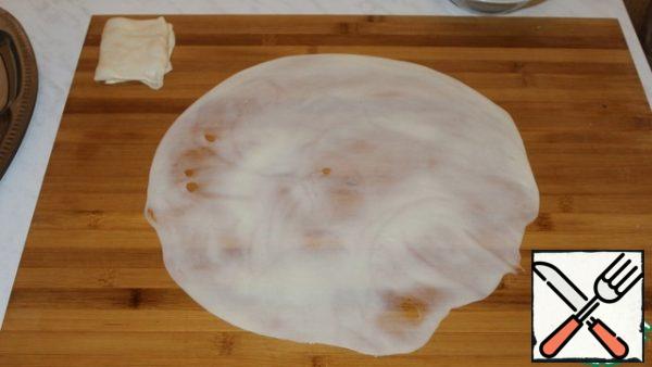 A piece of dough is stretched to transparency with hands smeared with vegetable oil.