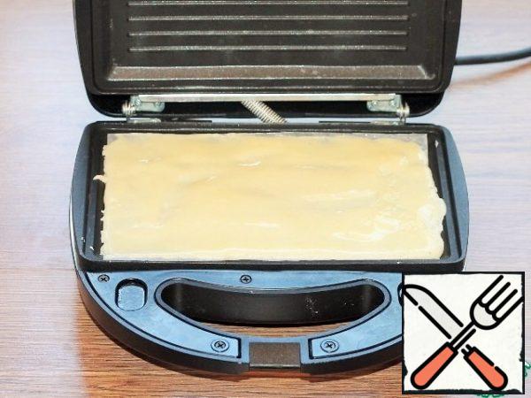 Open the lid of the slow cooker and cover with paper. lubricate it with vegetable oil. Spread the dough on the bottom panel of the device (2 tbsp.l.) and smooth with a wet silicone spatula. Close the lid.