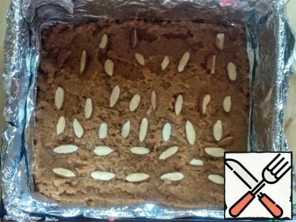 In the prepared form, put half of the cream of boiled condensed milk, sprinkle almonds on top.
