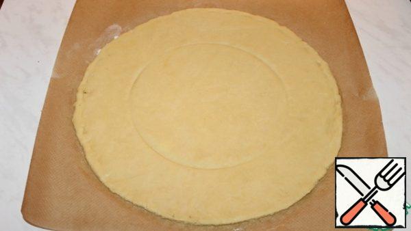 Roll out the dough on parchment into a circle with a diameter of 30-32 cm. In the center, mark a circle of smaller diameter.