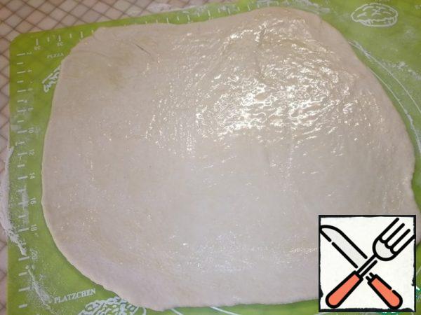 Divide the dough into three parts. Each part is thinly rolled out and smeared with melted butter.